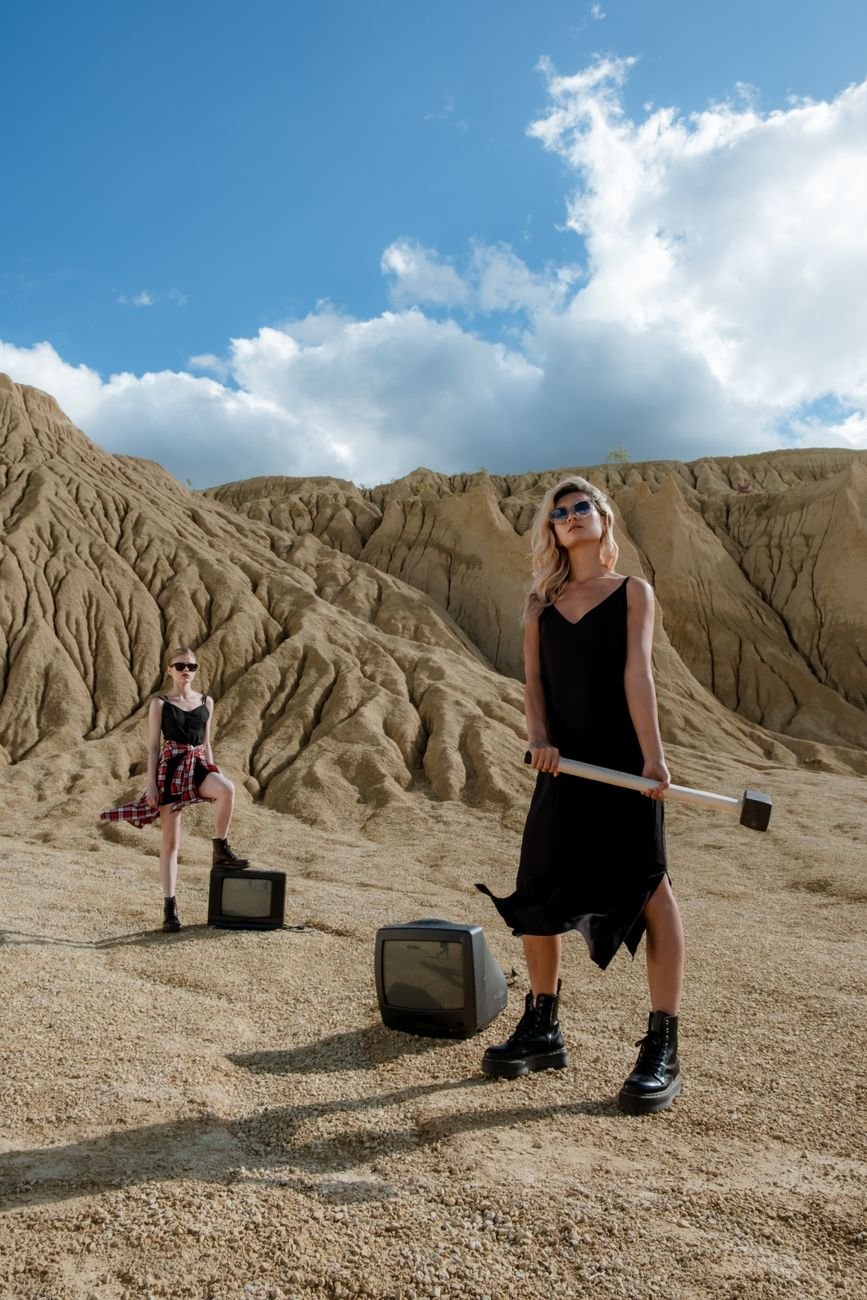 Stylish women in a desert with vintage TVs, blending fashion and landscape.